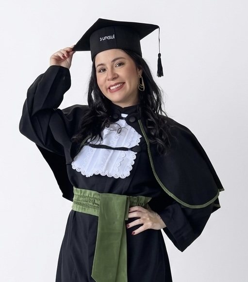 Priscilla sorrindo com beca e capelo em fundo claro