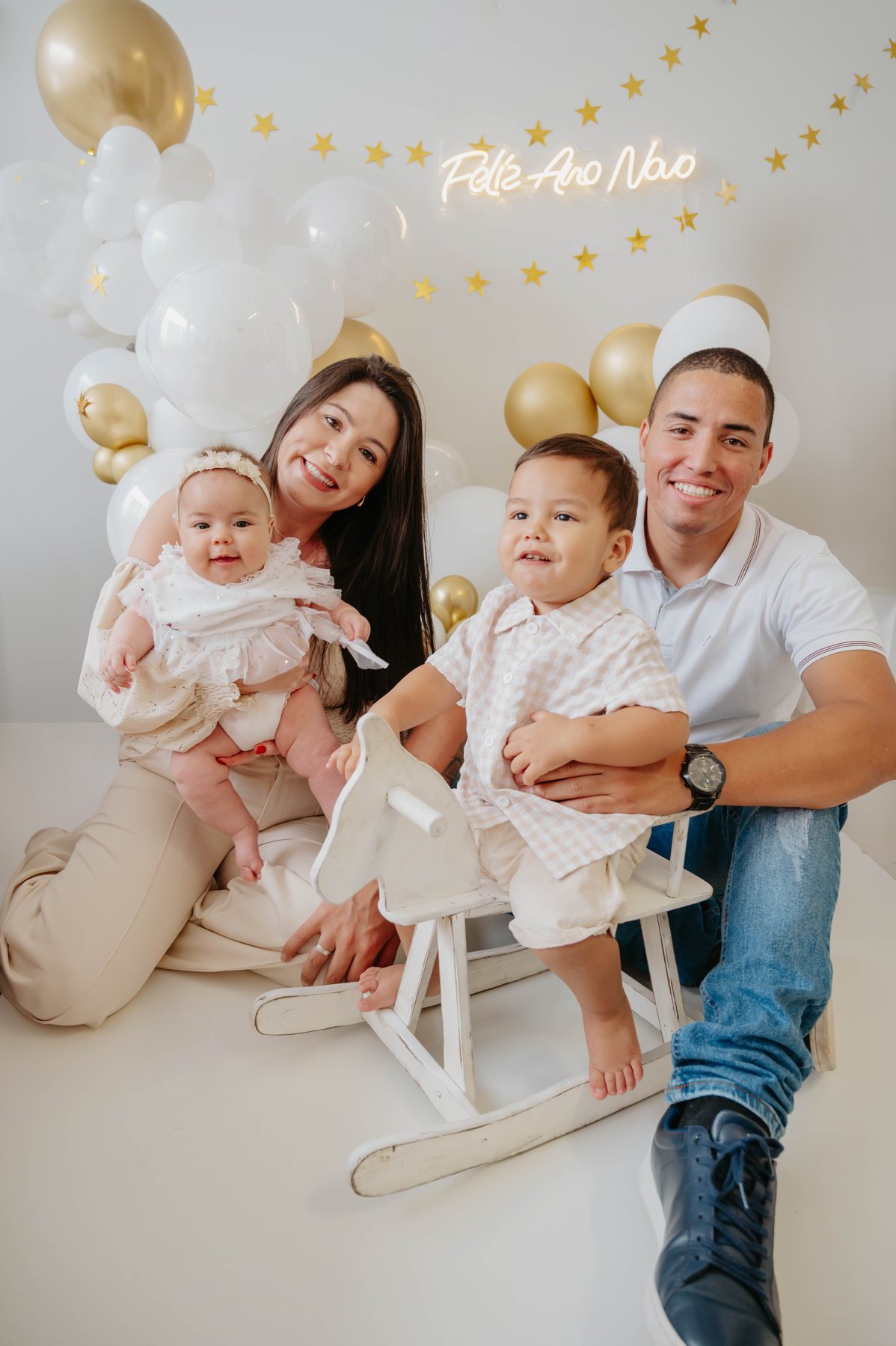 Priscilla, Henrique e as duas crianças sentados juntos em um ensaio claro com balões