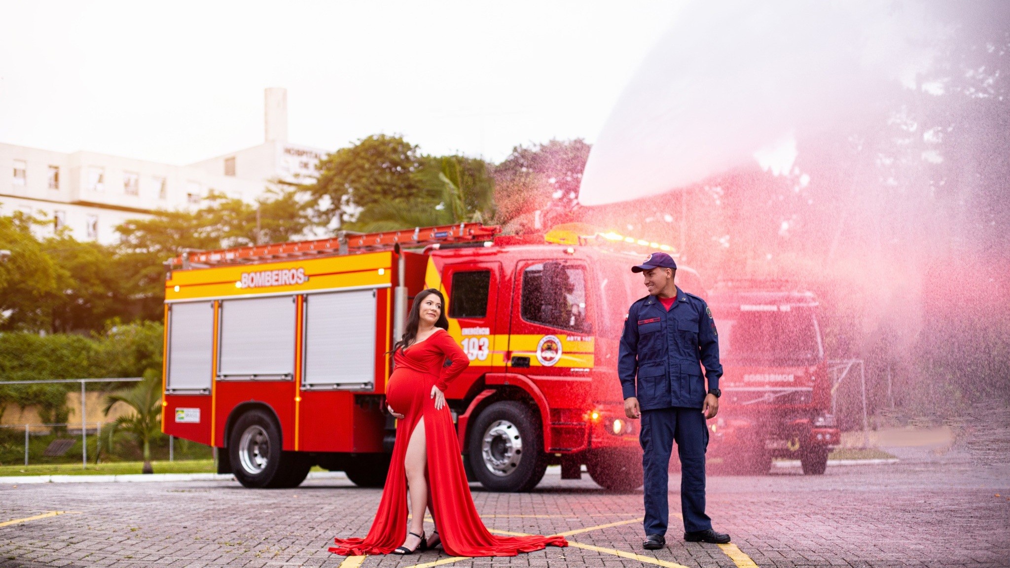 Priscilla, de vestido vermelho, e Henrique, de farda de bombeiro, ao lado de um caminhão dos Bombeiros com o número 193
